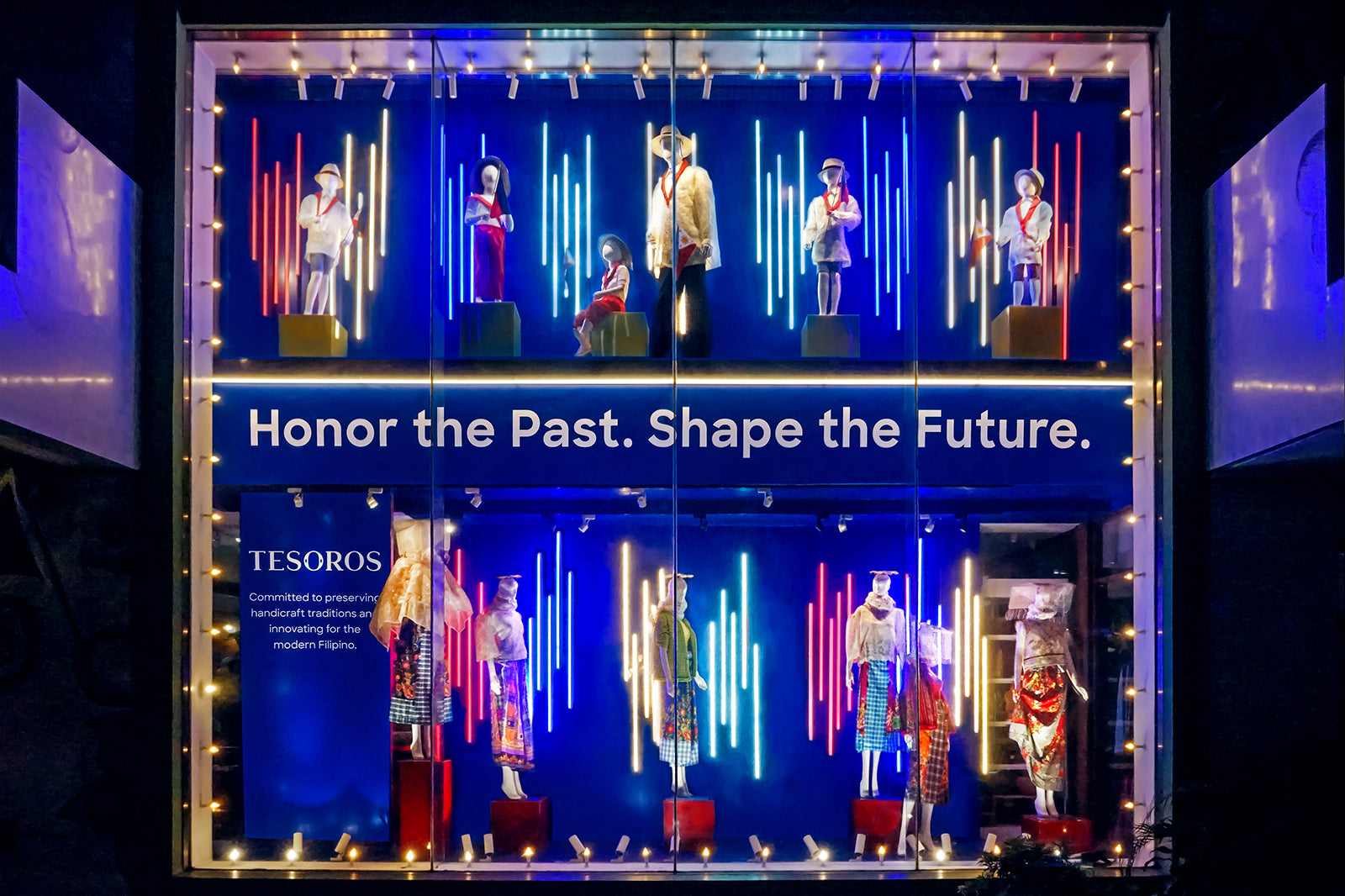 Store display with mannequins in traditional attire, neon lights, and text: Honor the Past. Shape the Future.